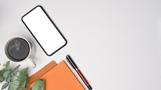 Vue de dessus du téléphone intelligent, de la tasse à café et du bloc-notes sur le bureau blanc.