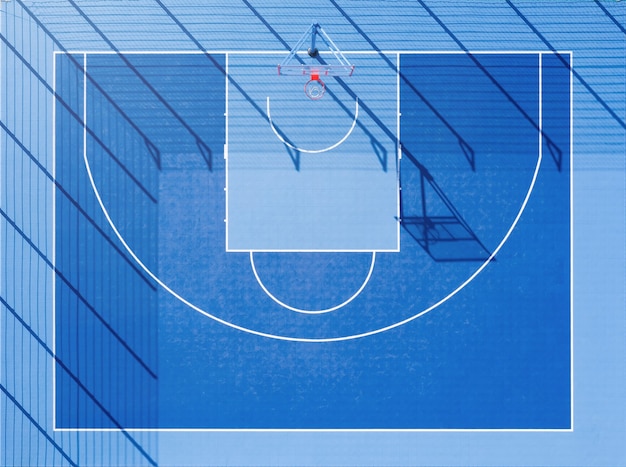 Vue de dessus du terrain de basket. Une cour bleue minimaliste avec de longues ombres à la lumière du jour depuis la vue aérienne.