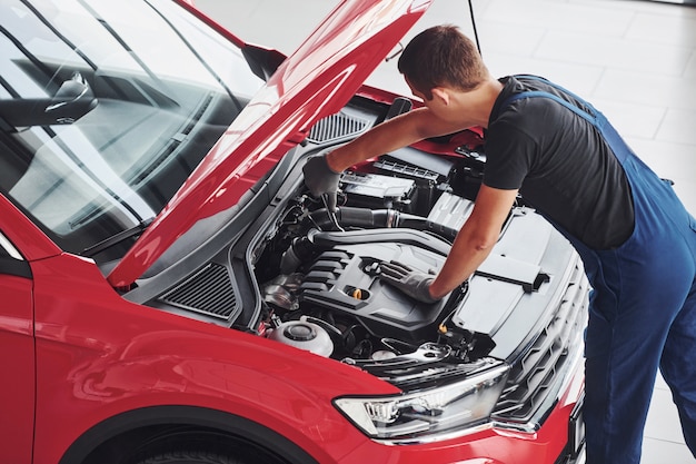 Photo vue de dessus du travailleur masculin en uniforme qui répare l'automobile rouge