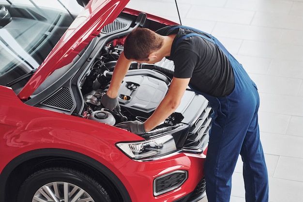 Vue de dessus du travailleur masculin en uniforme qui répare l'automobile rouge