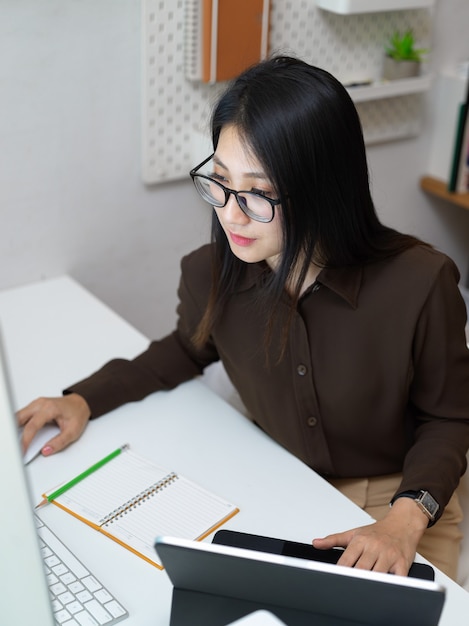 Vue de dessus d'une employée de bureau avec des lunettes se concentrant sur son travail avec des fournitures informatiques et de bureau