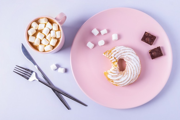 Vue de dessus encore la vie d'un gâteau mordu sur une assiette rose, des couverts et une tasse de cacao avec des guimauves. Mise au point sélective, orientation horizontale.