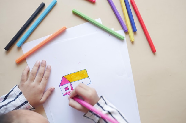 Vue de dessus d'enfant fille dessinant une maison avec des crayons de couleur sur papier