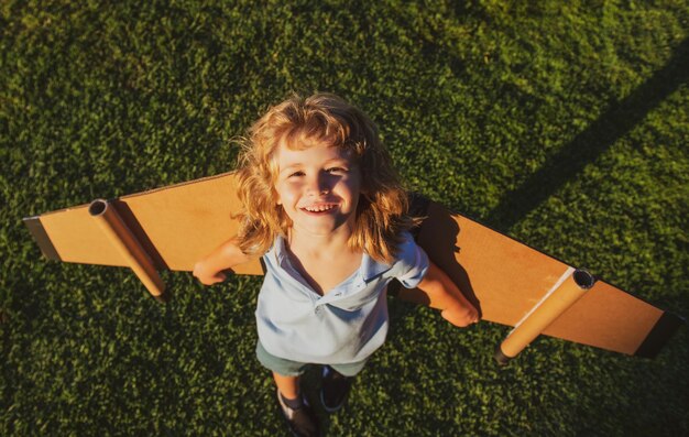 Vue de dessus enfant voyageur avec sac à dos ailes enfant jouant pilote aviateur et rêves à l'extérieur dans le parc