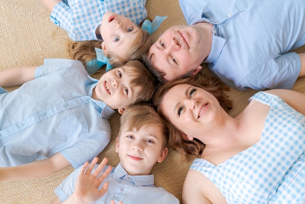 Vue de dessus des enfants mignons et leurs beaux jeunes parents regardant la caméra et souriant en position couchée...