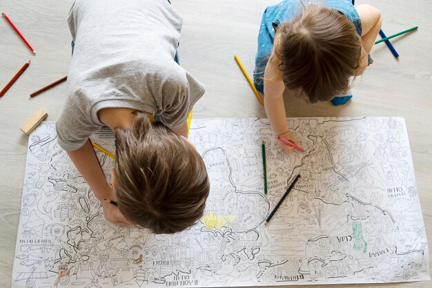 Vue de dessus d'enfants peignant un grand livre de coloriage sur le sol