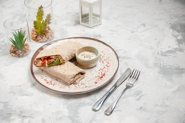 Vue de dessus de l'enveloppe de lavash et du yaourt dans un petit bol sur une assiette et des couverts de maison de jouets sur une surface blanche tachée