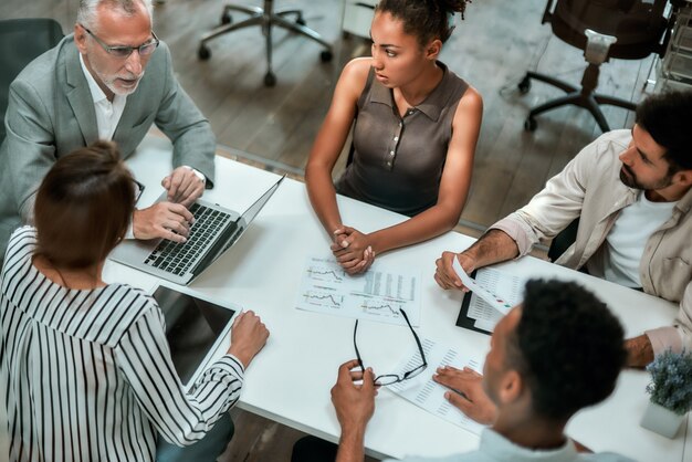 Vue de dessus de l'équipe multiculturelle discutant des affaires tout en étant assis à la table du bureau ensemble