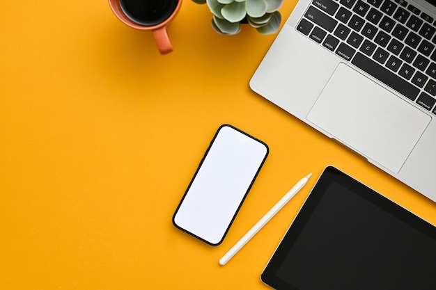 Vue de dessus d'un espace de travail de bureau créatif avec maquette de smartphone sur fond jaune