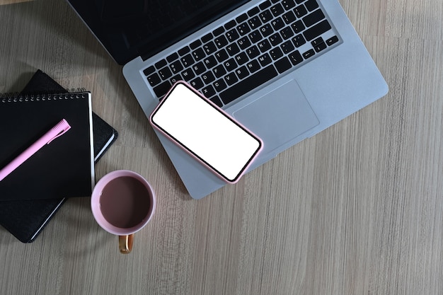 Vue de dessus de l'espace de travail design avec ordinateur portable à écran blanc, téléphone portable, tasse à café et ordinateur portable sur table en bois.