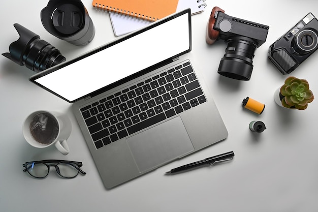 Vue de dessus de l'espace de travail du photographe avec une tasse de café et des verres de caméra d'ordinateur portable sur un tableau blanc