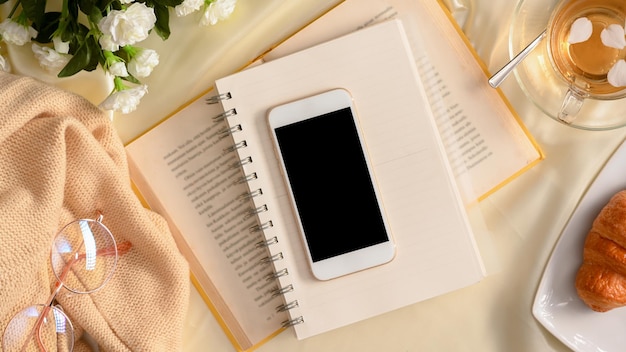 Vue de dessus de l'espace de travail féminin minimal Écran noir du smartphone sur un service à thé et un décor de livres romans
