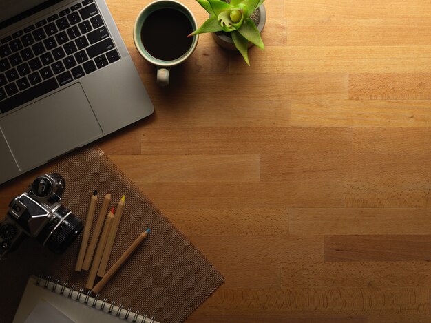 Vue de dessus de l'espace de travail avec ordinateur portable, appareil photo, papeterie et espace copie sur un bureau en bois