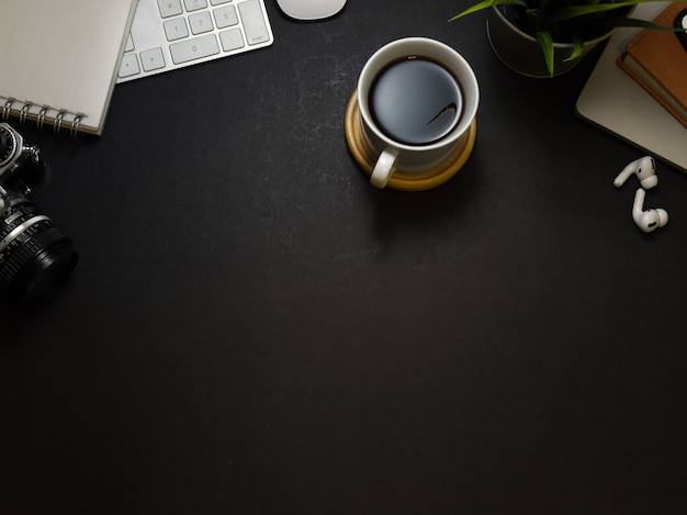 Vue de dessus de l'espace de travail sombre avec tasse à café, papeterie, écouteurs et espace copie, scène créative