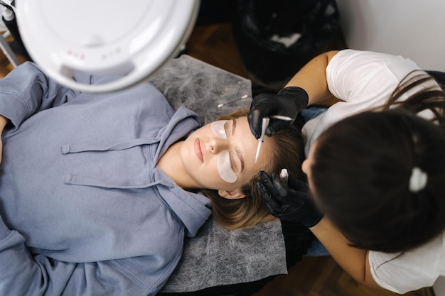 Vue de dessus d'une esthéticienne faisant des procédures de stratification de cils pour un jeune professionnel du modèle de cheveux blonds