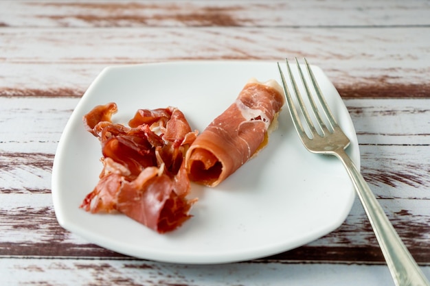 Vue de dessus d'un exquis jambon serrano espagnol avec une fourchette sur une assiette blanche.