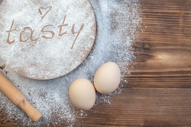 vue de dessus farine blanche avec oeufs et rouleau à pâtisserie sur table marron