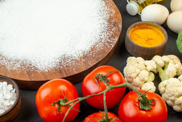 Vue de dessus de la farine sur planche de bois oeufs tombés bouteille d'huile tomates chou-fleur brocoli sur fond noir