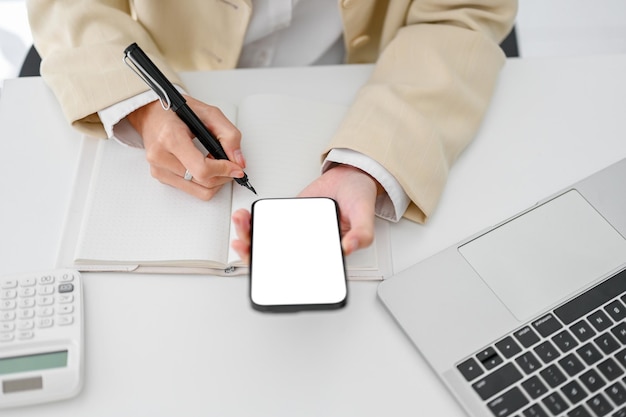 Vue de dessus d'une femme d'affaires utilisant son smartphone tout en prenant des notes sur son carnet