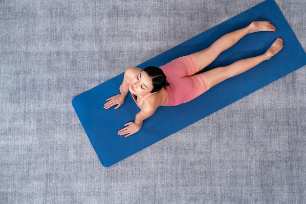 Vue de dessus femme asiatique en vêtements de sport faisant des exercices de yoga sur un tapis de fitness comme routine d'entraînement à domicile Soins du corps sains et méditation calme dans un style de vie de yoga Vigoureux