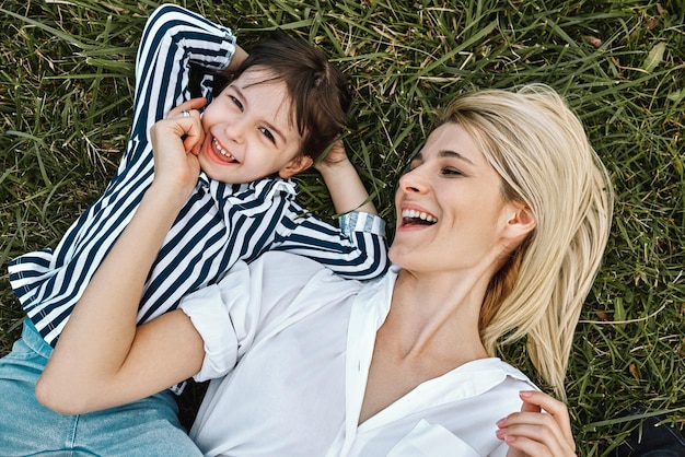 Vue de dessus d'une femme blonde heureuse souriant et jouant avec son mignon petit enfant allongé sur l'herbe verte en plein airLa mère et la fille aimantes passent du temps ensemble dans un parc Maman et enfant s'amusent Fête des mères