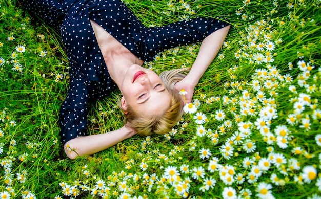 Vue de dessus de la femme blonde en robe noire couchée sur la prairie de fleurs de camomille