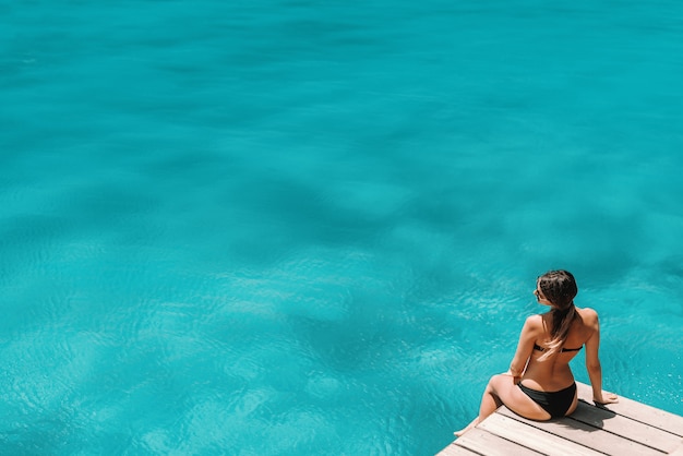 Vue de dessus d'une femme caucasienne assise sur le quai en bikini et posant. Concept de vacances d'été.