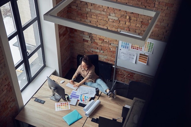 Vue de dessus d'une femme détendue en train de taper tout en travaillant sur un nouveau projet de design d'intérieur assis à