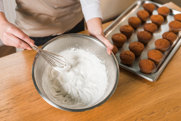 Une vue de dessus de femme fouettée blancs d&#39;oeufs avec un fouet pour faire de la crème dans le bol