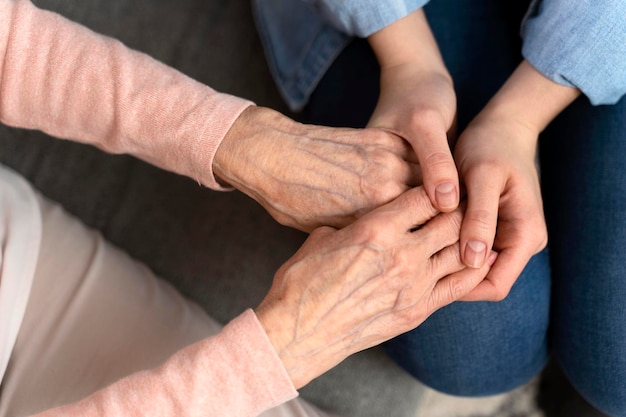 Vue de dessus de la femme mature âgée de la peau ridée et des mains de son soignant Une femme âgée dans un établissement de soins pour personnes âgées reçoit l'aide d'une infirmière du personnel hospitalier