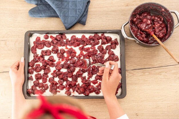 Vue de dessus d'une femme mettant des cerises cuites sur un glaçage à la crème d'un gâteau avec une cuillère.