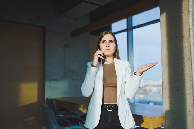 Vue de dessus d'une femme positive en vêtements décontractés debout près d'une grande fenêtre et parlant au téléphone donnant des informations pendant le projet à distance Espace de travail moderne pour le travail à distance