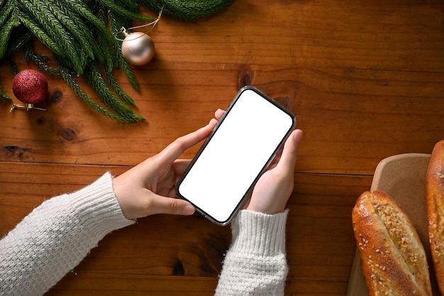 Vue de dessus Une femme tenant une maquette de smartphone sur son espace de travail sur le thème de Noël