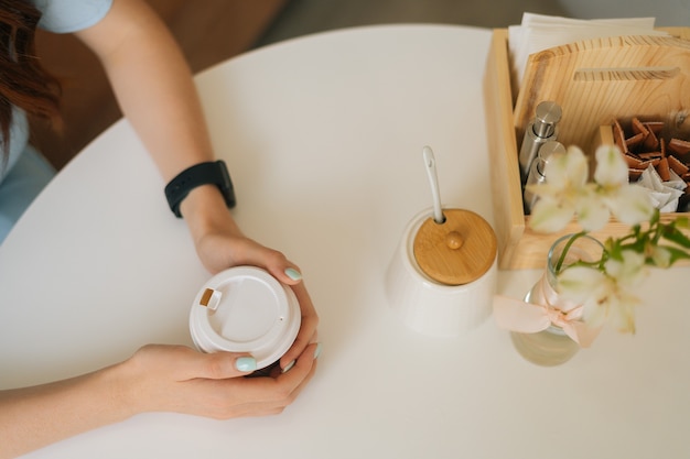 Vue de dessus d'une femme tenant une tasse de café chaud du matin assis à une table blanche dans un café confortable.