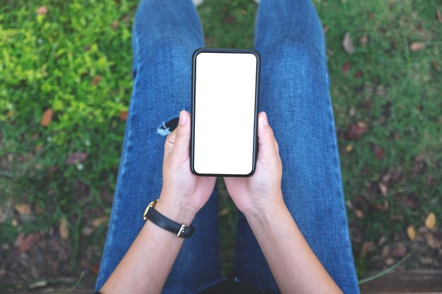 Vue de dessus femme tenant un téléphone mobile noir avec écran blanc vierge alors qu'il était assis dans le parc