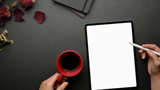 Vue de dessus de la femme travaillant avec une tablette numérique comprend un écran et une tasse de café sur un espace de travail créatif noir