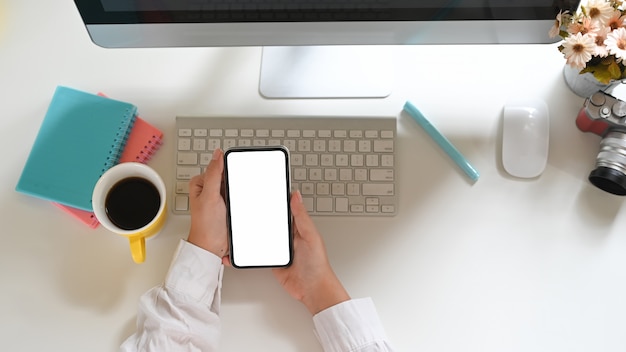 Vue de dessus femme utilise un smartphone à écran blanc alors qu'il était assis devant un écran d'ordinateur