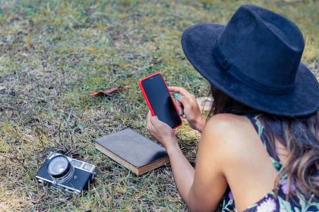 Vue de dessus d'une femme vêtue d'une robe noire et d'un chapeau regardant son smartphone allongé sur le ventre