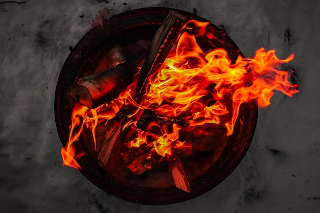 Vue de dessus d'un feu de camp dans un pot en métal entouré de neige lors d'une soirée d'hiver