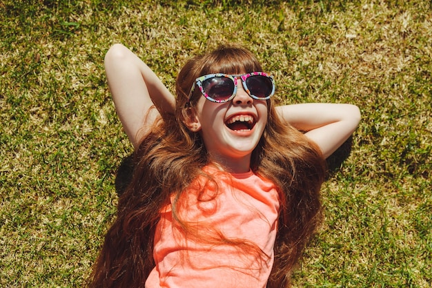 Vue de dessus d'une fille heureuse souriante et allongée sur l'herbe verte un jour d'été dans le parc