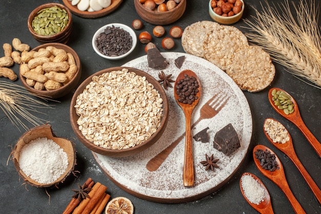 vue de dessus flocons d'avoine dans un bol en bois empreinte de fourche avec du sucre glace gouttes de chocolat noir dans une cuillère en bois craquelins de riz noix épis de blé sur table