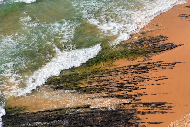 Vue de dessus sur les formations rocheuses sur la plage de Monte Clerigo et vague de surf avec de la mousse (Aljezur, Algarve, Portugal).