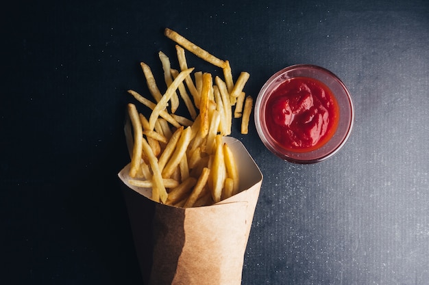 Vue de dessus de frites avec du ketchup sur fond noir.