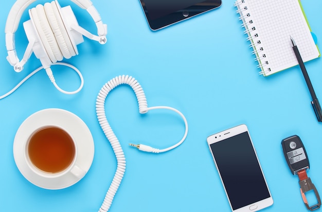 Vue de dessus sur les gadgets sur fond bleu, composition d'écouteurs blancs, téléphone, tablette, verre avec une boisson et clés de voiture