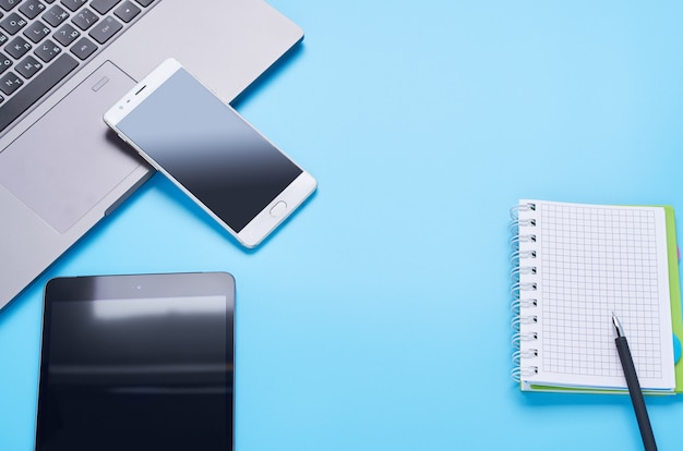 Vue de dessus sur les gadgets sur fond bleu, la composition d'un ordinateur portable, un casque blanc, un téléphone, un verre avec une boisson et des clés de voiture