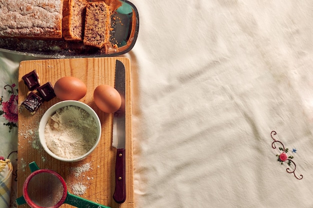 Vue de dessus d'un gâteau éponge fait maison sur une nappe blanche avec quelques ingrédients oeufs chocolat et farine