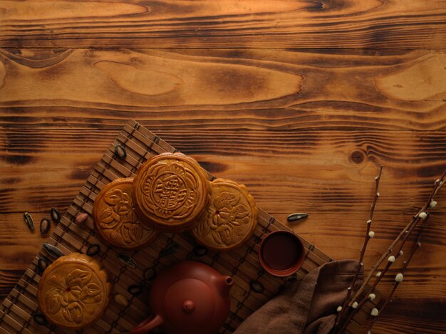 Vue de dessus des gâteaux de lune traditionnels sur tapis de bambou avec service à thé et espace copie sur table rustique. Le caractère chinois sur le gâteau de lune représente "cinq grains et du porc rôti" en anglais