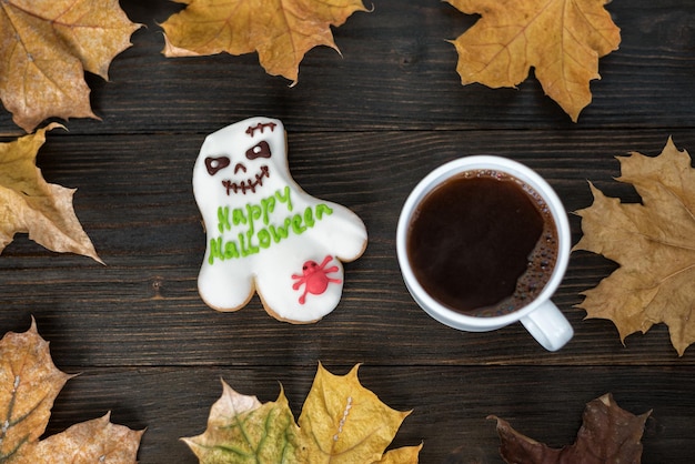 Vue de dessus Gingerbread like Ghost et tasse de café sur une table en bois à côté des feuilles d'automne Happy Halloween