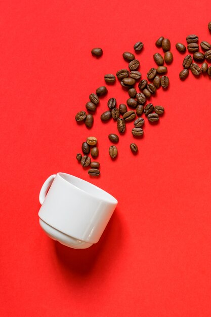 Vue de dessus des grains de café torréfiés frais et tasse blanche sur fond rouge. Mise à plat.