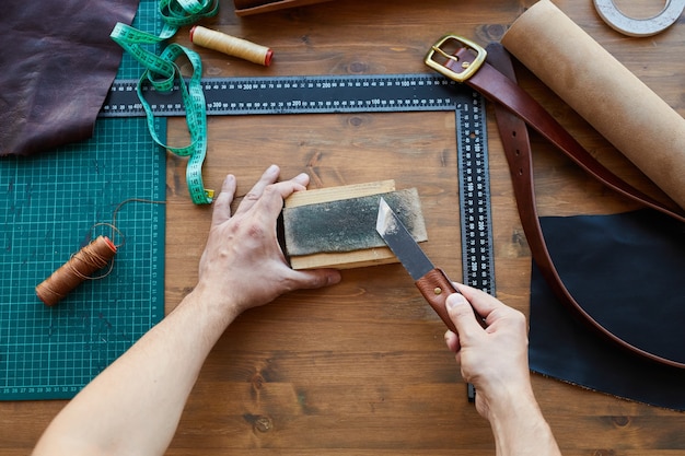 Vue de dessus en gros plan d'un artisan masculin méconnaissable travaillant avec du cuir dans un atelier d'artisanat...